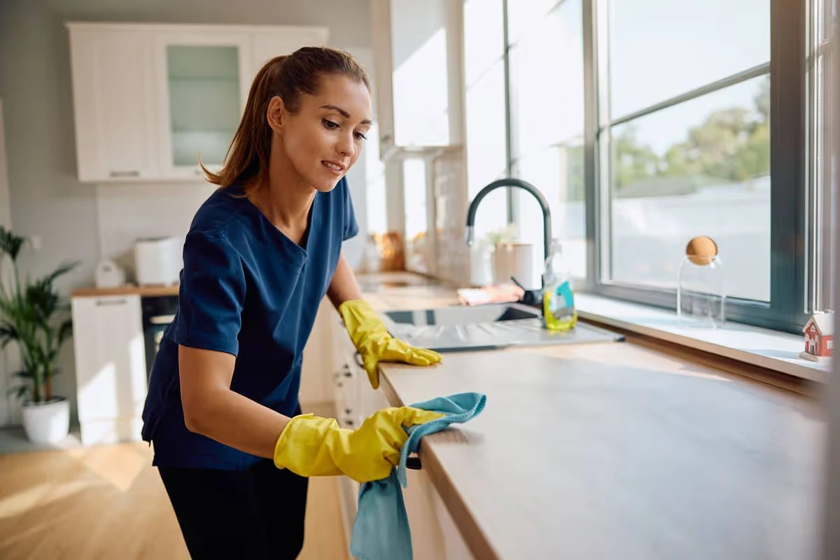 A cleaner wiping down a bright residential kitchen